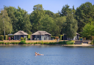 Small cabins by the lake at Holiday park Tolplas 19 in the Netherlands, surrounded by trees and greenery.