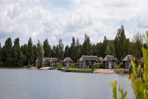 Udsigt over søen til feriehusene i Holiday park Tolplas 19, Holland, med træer i baggrunden.