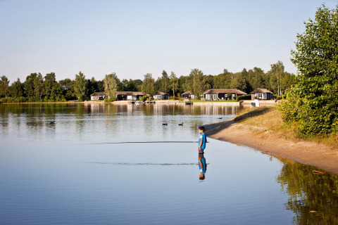Un garçon se tient dans l'eau peu profonde devant de petites maisons au Holiday park Tolplas 19, Pays-Bas.