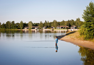 Un niño está parado en agua poco profunda cerca de casas pequeñas en Holiday park Tolplas 19, Países Bajos.