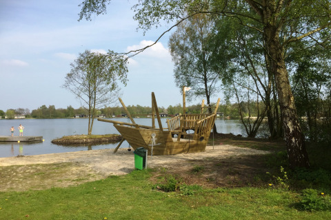Legeplads med et træpiratskib ved søbredden i ferieparken Tolplas 19, Holland, omgivet af natur.