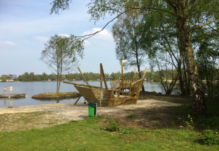 Legeplads med et træpiratskib ved søbredden i ferieparken Tolplas 19, Holland, omgivet af natur.