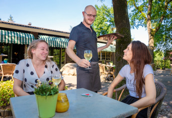 Zwei Frauen bekommen draußen Weißwein von einem Kellner im Holiday Park Tolplas 19 in den Niederlanden.