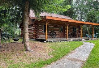 Image of a cozy American Log Cabin chalet with porch, barbecue, and lawn chairs in a wooded area in the Netherlands.
