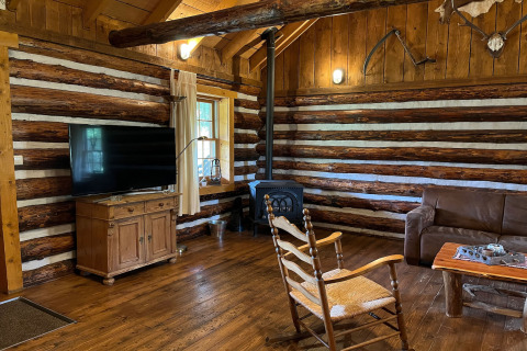 Salon du chalet American Log Cabin aux Pays-Bas avec poêle à bois, meubles rustiques et télévision.