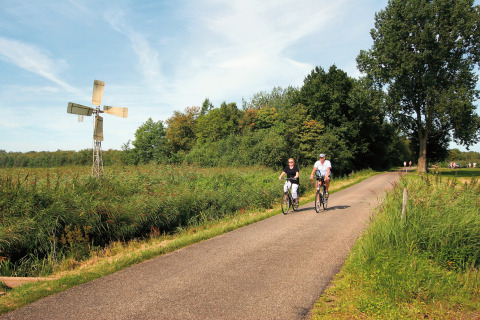 Due persone in bicicletta su una strada di campagna vicino a una piccola pala eolica a Tolplas 19, Paesi Bassi.