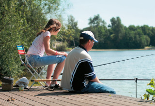 Un hombre y una niña pescando juntos en un muelle de madera junto al lago en Holiday park «Tolplas 19» en los Países Bajos.