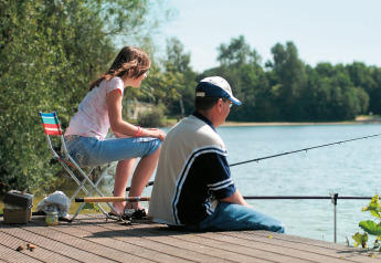 A man and a girl fishing together on a wooden pier by the lake at Holiday park «Tolplas 19» in the Netherlands.