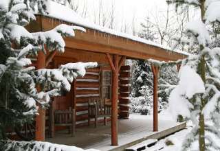 Blockhütte namens American Log Cabin in den Niederlanden, umgeben von verschneiten Bäumen.