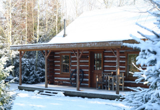 Chalet americano di tronchi innevato nei Paesi Bassi, con veranda rustica e alberi tutt'intorno.