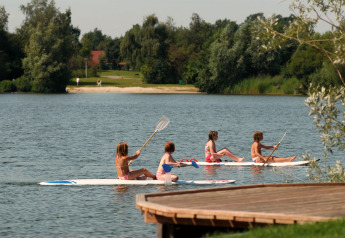 Vier Kinder paddeln sitzend auf Boards auf dem See im Holiday Park Tolplas 19, Niederlande.