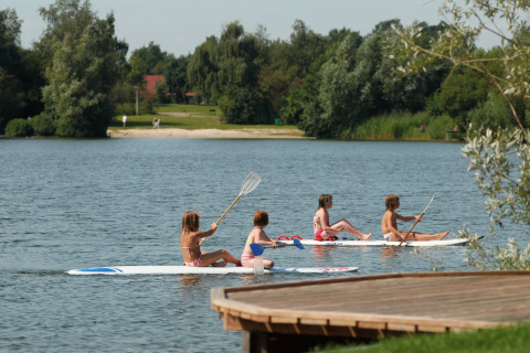 Quattro bambini seduti su paddleboard sul lago vicino a Holiday park Tolplas 19, circondati dalla natura olandese.