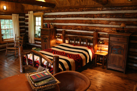 Dormitorio acogedor en una cabaña de troncos americana con muebles rústicos y manta estampada.