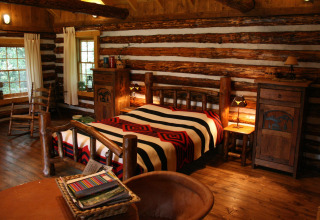 Cozy bedroom in an American log cabin with rustic wooden furniture, large bed, and patterned blanket.
