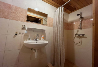 Bagno con doccia, lavandino, specchio e dettagli in legno presso lo chalet American Log Cabin nei Paesi Bassi.
