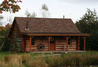 Amerikanische Blockhütte mit Veranda und Schindeldach, umgeben von Bäumen in den Niederlanden.