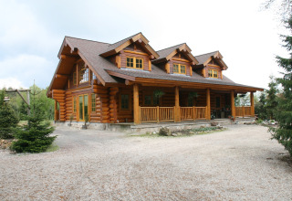 Foto di uno chalet American Log Cabin con veranda, circondato da alberi, scattata nei Paesi Bassi.