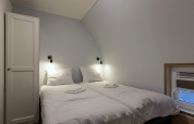 Helles Schlafzimmer mit zwei Einzelbetten, weißen Laken und Nachttischlampen in Residence De Eese 22.