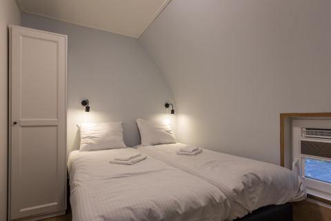 Lyst værelse med to enkeltsenge, hvidt sengetøj, natlamper og skab i Residence De Eese 22 i Holland.