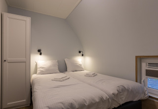 Lyst værelse med to enkeltsenge, hvidt sengetøj, natlamper og skab i Residence De Eese 22 i Holland.