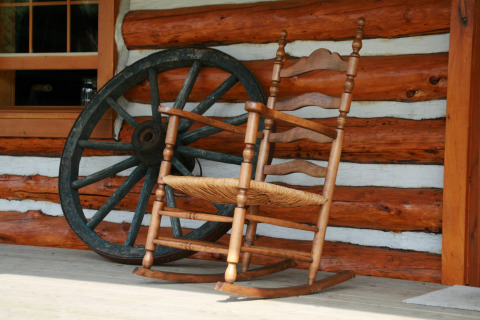 Une chaise berçante et une roue de chariot sur le porche à American Log Cabin aux Pays-Bas.