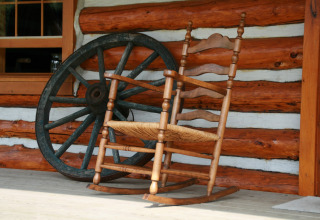 Una mecedora y una rueda de carro ante una cabaña en American Log Cabin en los Países Bajos.