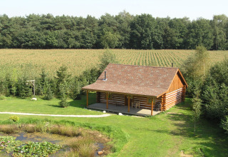 Chalet American Log Cabin aux Pays-Bas dans un cadre rural avec champs, forêt et petit étang devant.