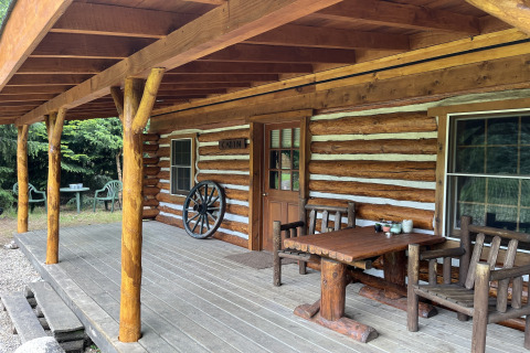 Véranda en bois d’un chalet américain aux Pays-Bas avec mobilier rustique et roue de chariot décorative.