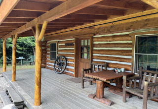 Porche de madera de una cabaña americana de troncos en los Países Bajos con muebles rústicos y naturaleza.