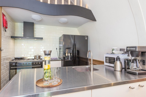 Moderne køkkenindretning med sort køleskab, stålbordplade, komfur og kaffemaskine i Residence De Eese 22.