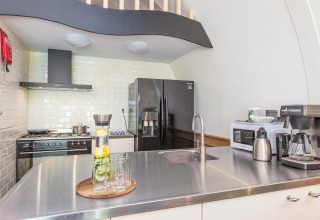 Moderne køkkenindretning med sort køleskab, stålbordplade, komfur og kaffemaskine i Residence De Eese 22.