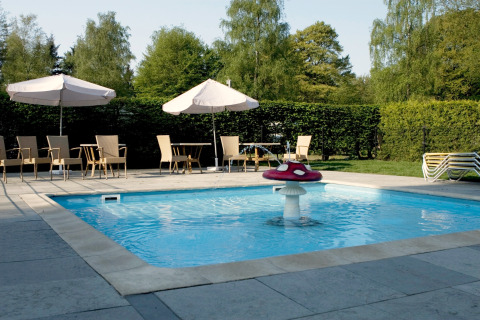 Buitenzwembad met paddenstoelfontein, parasols en tuinmeubels bij een glampingverblijf in de zomer.
