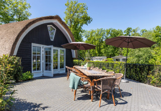Buitenterras van Residence De Eese 22 in Nederland met tafel, stoelen en twee grote parasols buiten.