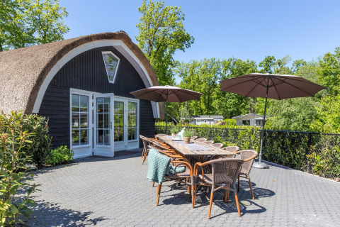 Udendørs terrasse ved Residence De Eese 22 i Holland med borde, stole og parasoller omgivet af natur.