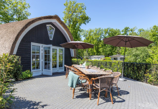 Udendørs terrasse ved Residence De Eese 22 i Holland med borde, stole og parasoller omgivet af natur.