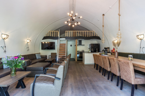 Moderne lodge opholdsstue med døbt loft, stort spisebord, loungeområde og køkken i Residence De Eese.