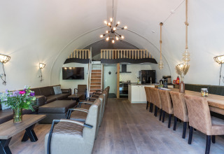 Moderne lodge opholdsstue med døbt loft, stort spisebord, loungeområde og køkken i Residence De Eese.