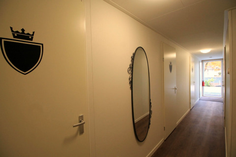 Hal bij Residence De Eese 22, Nederland, met ovale spiegel en deuren met schild en kroonsymbool.