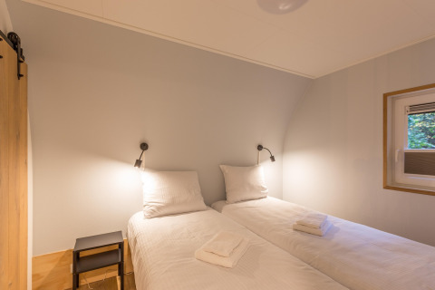 To enkeltsenge med hvidt sengetøj og væglamper på et værelse i Residence De Eese 22, Nederlandene.