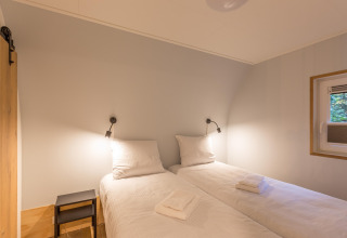 To enkeltsenge med hvidt sengetøj og væglamper på et værelse i Residence De Eese 22, Nederlandene.