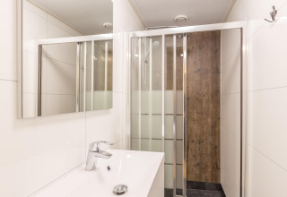 Moderne badeværelse på Residence De Eese 22 i Holland med brusekabine, spejl og hvid vask.