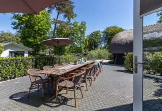 Udendørs spiseområde med lang træbord, stole og parasoller på Residence De Eese 22 i Holland.