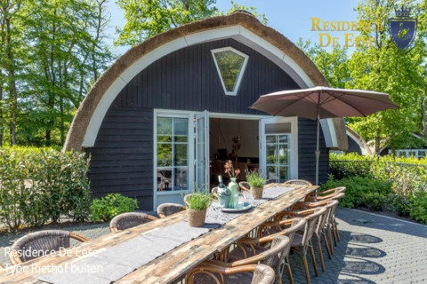 Buitenruimte bij lodge Residence De Eese 22 in Nederland met lange tafel en grote parasol.