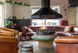 Knusse lounge met centrale haard, lederen stoelen en rode zetel in Residence De Eese 22, Nederland.