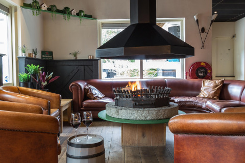 Hyggelig lounge med pejs i centrum, lænestole i læder og rød sofasæt, Residence De Eese 22, Holland.