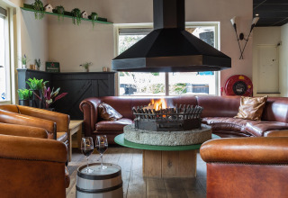 Hyggelig lounge med pejs i centrum, lænestole i læder og rød sofasæt, Residence De Eese 22, Holland.