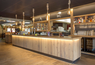 Moderne bar in Residence De Eese 22, Nederland, met houten toog, wijnrek en hanglampen.