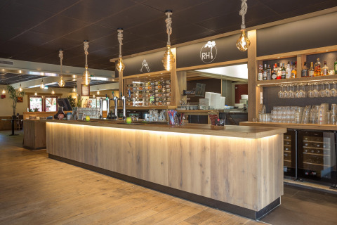Moderne bar i Residence De Eese 22 med træborde, hængende lamper og vinflasker i Holland.