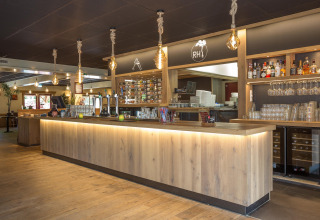 Moderne bar i Residence De Eese 22 med træborde, hængende lamper og vinflasker i Holland.