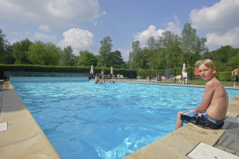 Dreng sidder ved swimmingpoolens kant på Residence De Eese 22, en lodge i Holland, omgivet af natur.